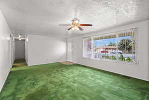 Spacious living area featuring expansive windows, green carpeting, a ceiling fan with integrated lighting, and a white entry door with decorative glass