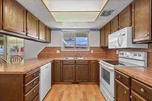 U-shaped kitchen featuring wood-finish flooring, wood-finish countertops, wood cabinetry, a double basin sink, and white appliances