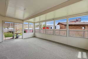 Enclosed sunroom featuring a textured carpet floor, white paneled walls, and a white paneled ceiling