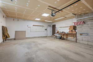 Spacious garage featuring a concrete floor, exposed ceiling joists, overhead lighting, an interior door, and a concrete block wall