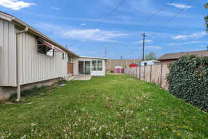Expansive lawn area with a sunroom addition, brick accent wall, and perimeter fencing
