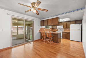 Kitchen featuring wood-finish flooring, wood cabinetry, white appliances, a breakfast bar, and a skylight