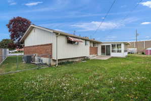 Rear exterior featuring a sunroom addition with multiple windows, a concrete patio, and a chain-link fence