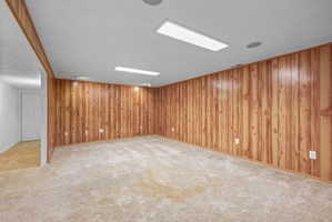 Spacious room featuring wood-panel walls and light-colored carpeting
