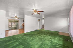 Spacious interior featuring a green carpeted area, white painted walls, and two ceiling fans