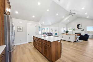 Kitchen with stainless steel refrigerator with ice dispenser, open floor plan, a warm lit fireplace, wood finish cabinetry, and light wood-type flooring