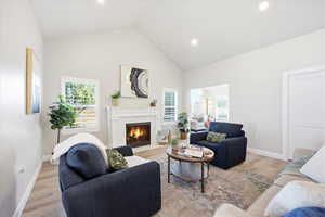 Living room with light wood-type flooring, a fireplace with flush hearth, lofted ceiling, plenty of natural light, and recessed lighting