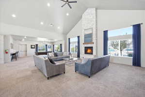 Living room with light carpet, a ceiling fan, a chandelier, lofted ceiling, and a stone fireplace