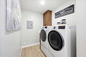Laundry area with light wood-style flooring, electric panel, cabinet space, and separate washer and dryer