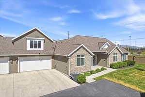 View of front facade with stone siding, stucco siding, a shingled roof, concrete driveway, and a front lawn
