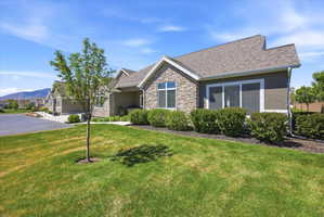 View of front of home with stone siding, a front yard, a shingled roof, and stucco siding