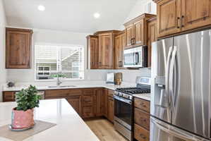 Kitchen featuring stainless steel appliances, wood finish cabinetry, light stone countertops, recessed lighting, and light wood-style flooring