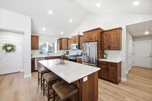 Kitchen featuring stainless steel appliances, a center island, a kitchen breakfast bar, light wood-type flooring, and light stone counters
