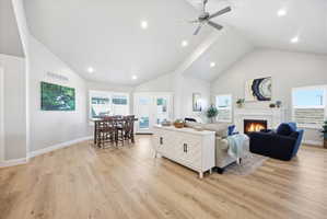 Living room featuring a lit fireplace, a high ceiling, light wood finished floors, ceiling fan, and recessed lighting