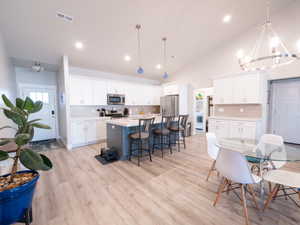 Open-concept kitchen and dining area featuring light wood-finish flooring, a vaulted ceiling, and recessed lighting
