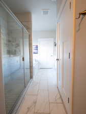 Spacious bathroom featuring large format marble-look floor tiles, a clear glass enclosed shower, and a built-in soaking tub