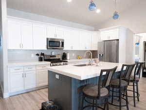 Modern kitchen featuring white shaker cabinetry, stainless steel appliances, a light gray subway tile backsplash, light wood-finish flooring, and a central island with a light-toned countertop