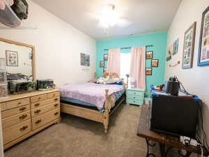 Carpeted bedroom featuring a light wood-finish bed frame, a matching wood-finish dresser with a large mirror, a ceiling fan with light, and a window with a light-colored accent wall
