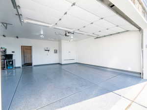 Spacious garage featuring a durable epoxy-coated floor, integrated ceiling lighting, white overhead garage door, built-in storage cabinetry, and a service door