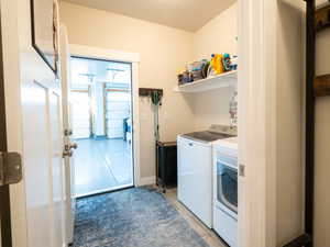 Dedicated laundry area featuring a white floating shelf, light wood-finish flooring, and a doorway opening to a garage with two overhead doors