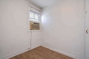 Bright interior space featuring a window with integrated air conditioning unit, white walls, and wood-finish flooring