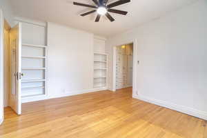 Hardwood flooring paired with built-in shelving, a ceiling fan, and white baseboards