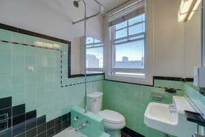 Bathroom featuring mint green and black tile work, a white pedestal sink, and a window with horizontal blinds