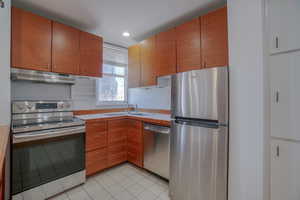 Modern kitchen featuring wood-finish cabinetry, stainless steel appliances, and white tile flooring