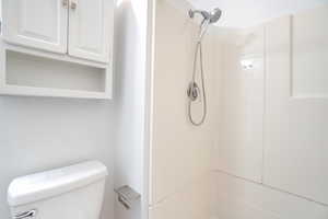 Bathroom featuring a white toilet, white cabinetry with an open shelf, and a shower-over-tub combination with a wall-mounted showerhead