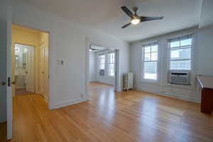 Hardwood flooring extending throughout, featuring multiple windows with natural light, and a ceiling fan with integrated lighting