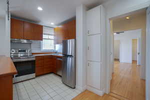 Kitchen featuring wood cabinetry, stainless steel appliances, tile flooring, recessed lighting, and built-in storage cabinets