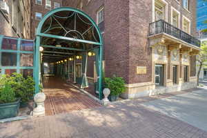 Architectural brick building facade featuring a covered entry, decorative iron balcony, ornamental building accents, and an arched glass canopy
