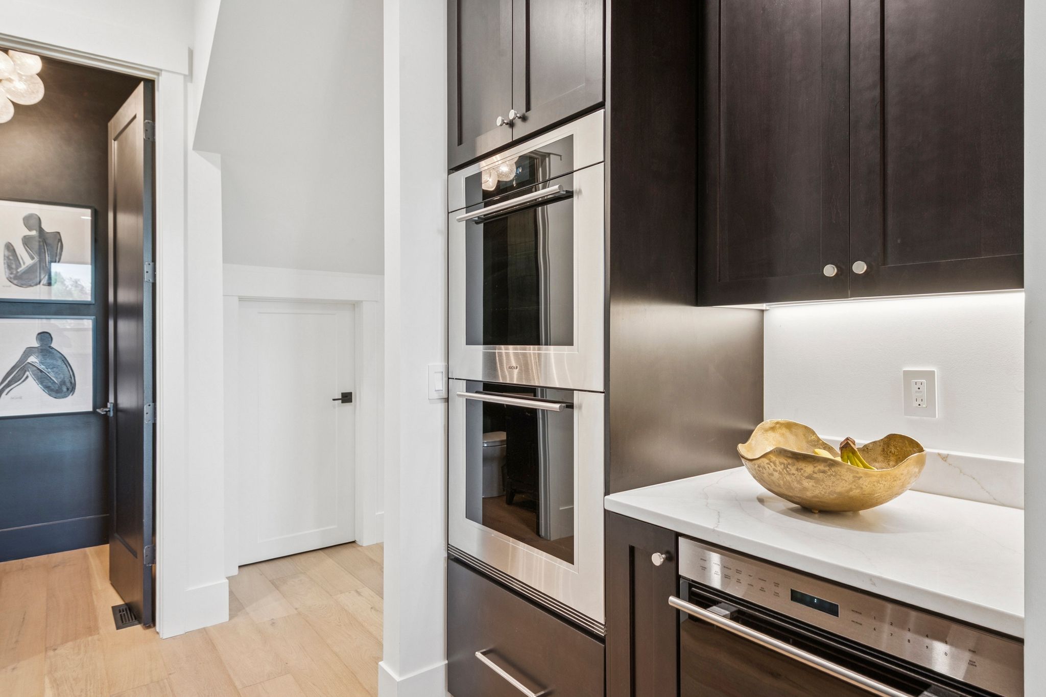 Wolf double ovens and microwave, dark wood-finish cabinetry, and quartz countertops with under-cabinet lighting.