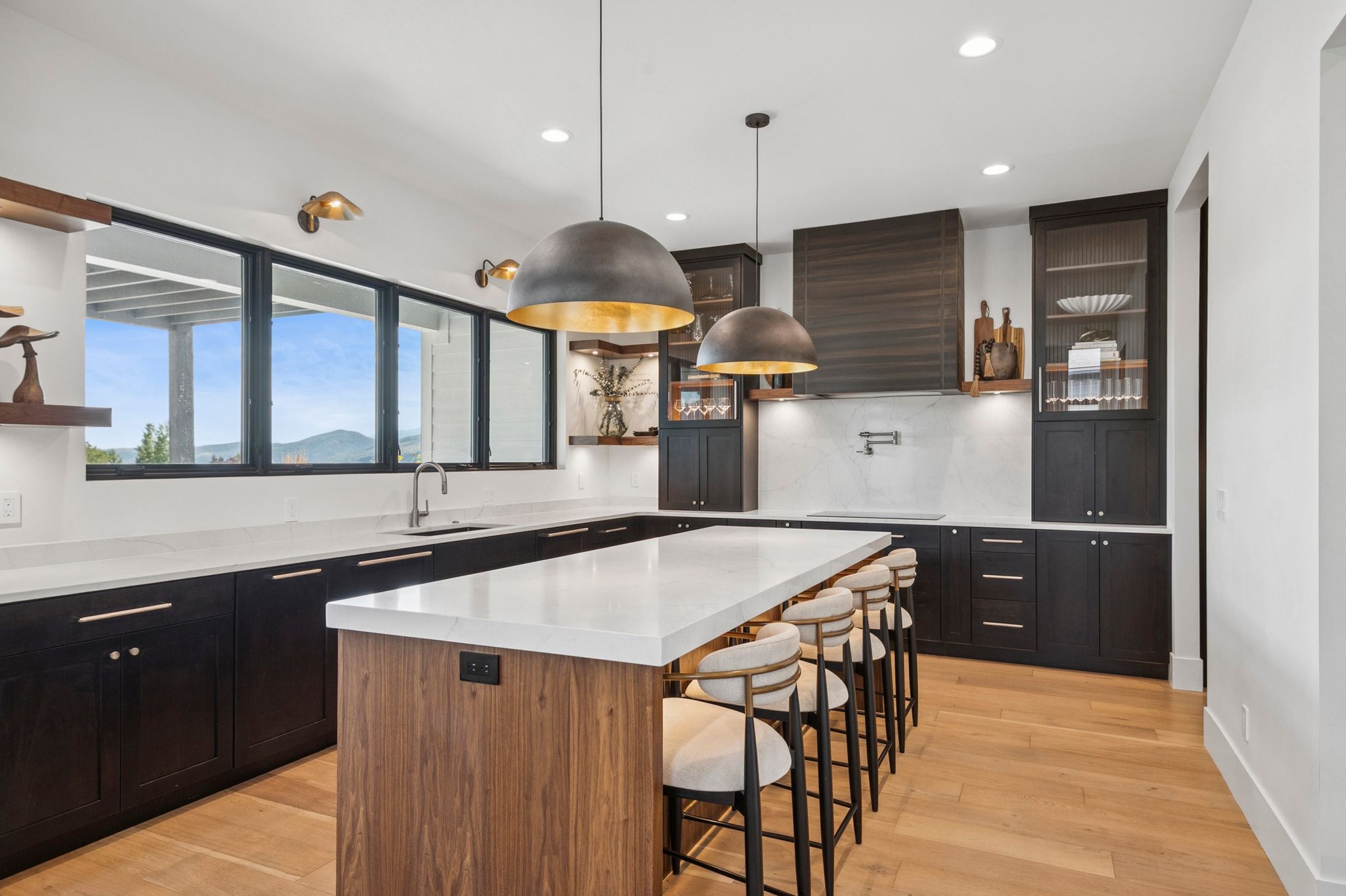 Spacious kitchen featuring a large island walnut cabinetry, and light hardwood flooring, designer lighting, with Wolf and Sub-Zero appliances.