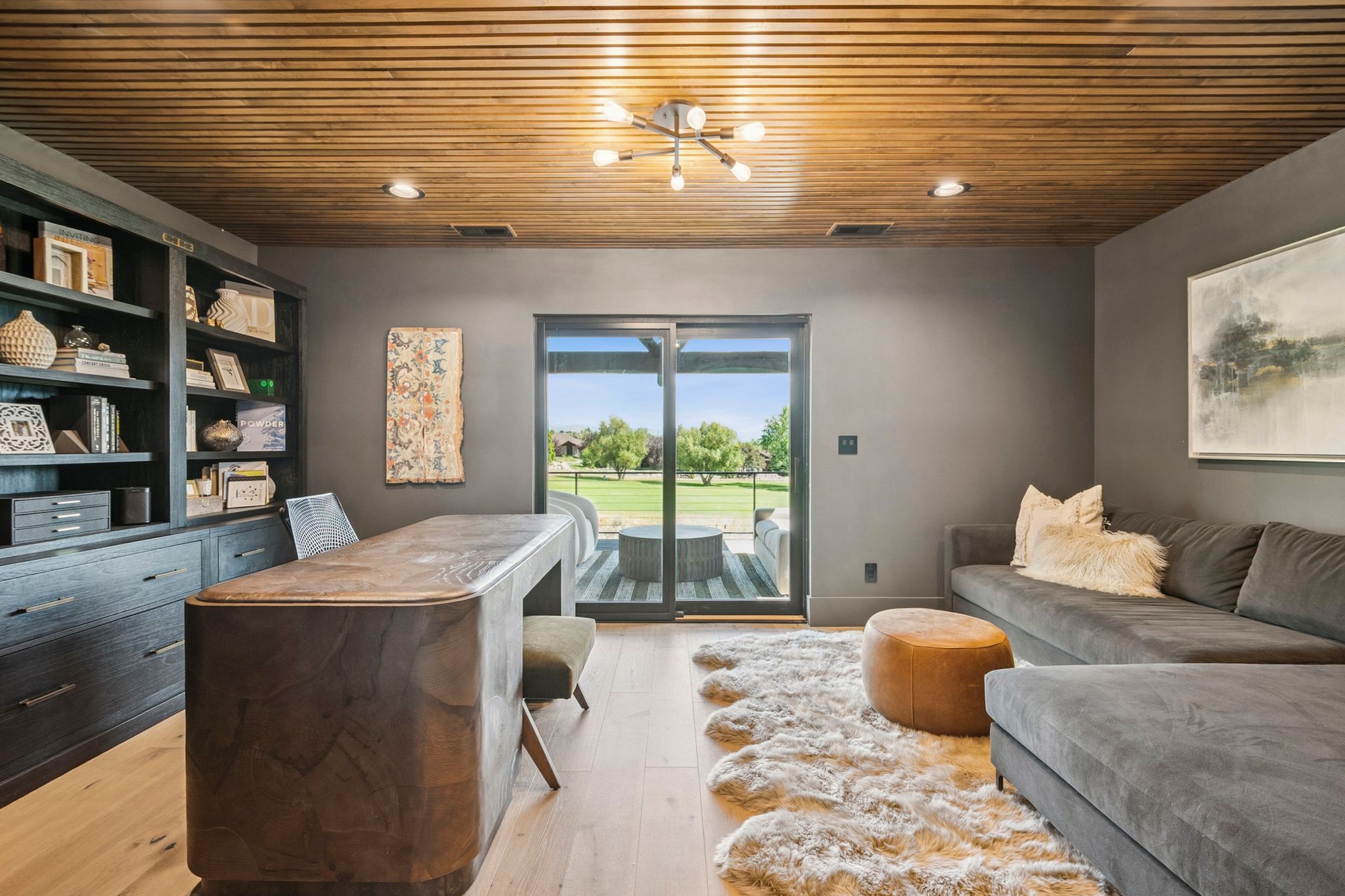 Stunning designer office with slatted wood ceiling, bookcases, and slider that opens to covered deck.