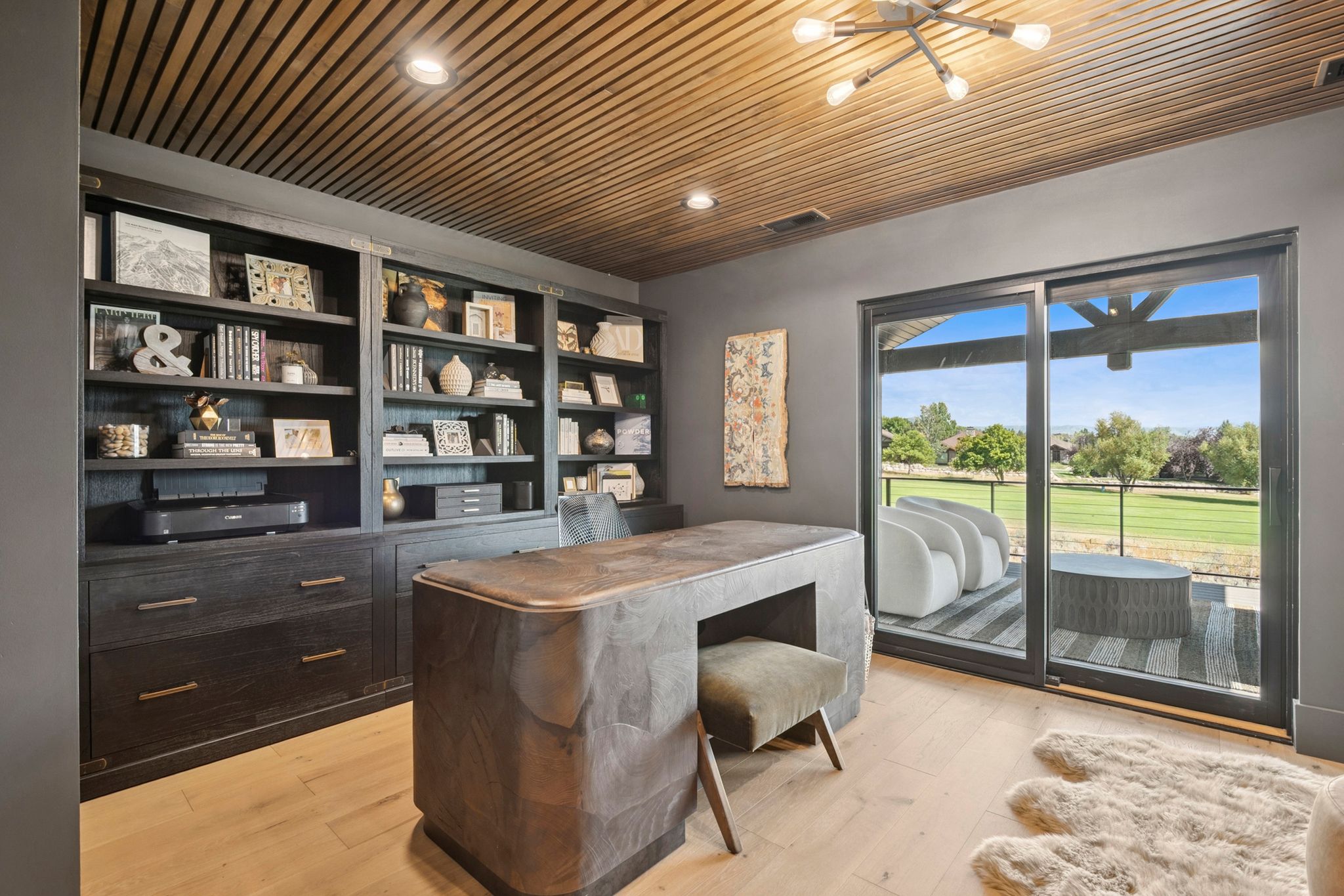 Stunning designer office with slatted wood ceiling, bookcases, and slider that opens to covered deck.