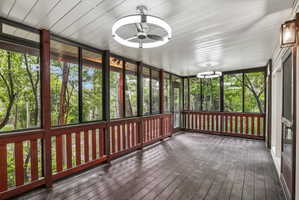 Expansive screened porch featuring dark wood-finish flooring, white paneled ceiling, two contemporary ceiling fans with integrated lighting, a wall-mounted exterior lantern, and full-height screens with wood railing