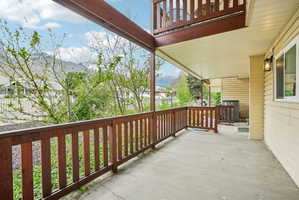 Covered concrete patio with wood railing, recessed lighting, and wall-mounted exterior fixtures