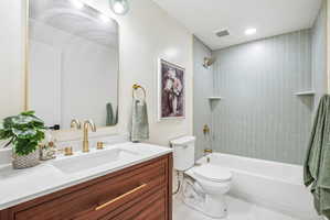 Bathroom featuring a wood-finish vanity with a white countertop and rectangular undermount sink, brushed gold hardware and faucet, and a shower-tub combination with light green subway tile surround and integrated shelving