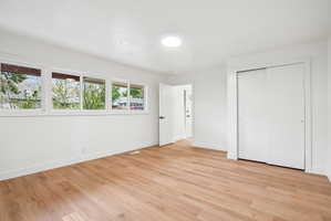 Spacious room featuring wood-finish flooring, white walls, and bright overhead lighting