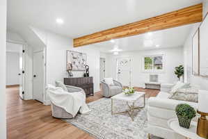 Spacious living area featuring wood-finish flooring, a prominent exposed wood beam, white walls, and recessed lighting