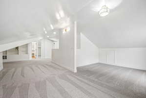Spacious loft area featuring sloped ceilings, recessed lighting, wall-mounted sconces, built-in shelving, and light gray patterned carpeting