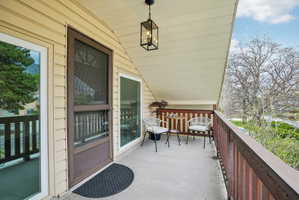 Covered outdoor balcony featuring tan siding and a dark brown door with an upper screen panel