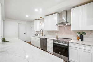 Kitchen featuring white shaker cabinetry, light-toned countertops with subtle veining, a stainless steel range with matching hood vent, a stainless steel dishwasher, and a gold-toned gooseneck faucet