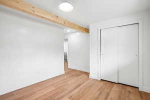 Room featuring wood-finish flooring, a prominent exposed wood beam, white walls, and a ceiling-mounted light fixture