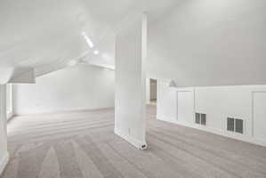 Spacious attic space featuring sloped ceilings, recessed lighting, neutral-toned carpet, built-in access panels, and baseboard trim
