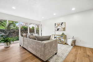 Bright living space featuring large picture windows, wood-finish flooring, recessed lighting, and crisp white walls