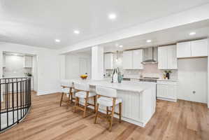 Modern kitchen featuring a large central island with seating, white shaker cabinetry, stainless steel appliances, and wood-finish flooring