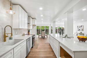 Contemporary kitchen featuring white cabinetry, light-toned countertops, a gold-finish faucet, recessed lighting, and wood-finish flooring