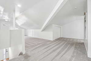 Spacious carpeted room featuring an angled ceiling, recessed lighting, built-in shelving, and a white sliding closet door
